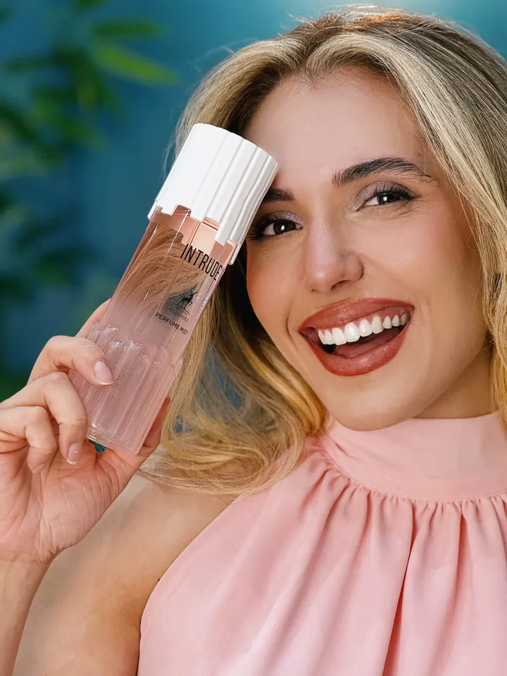 Mulher sorrindo com o Perfume Mist Intrude, da Maison Alhambra, junto ao rosto